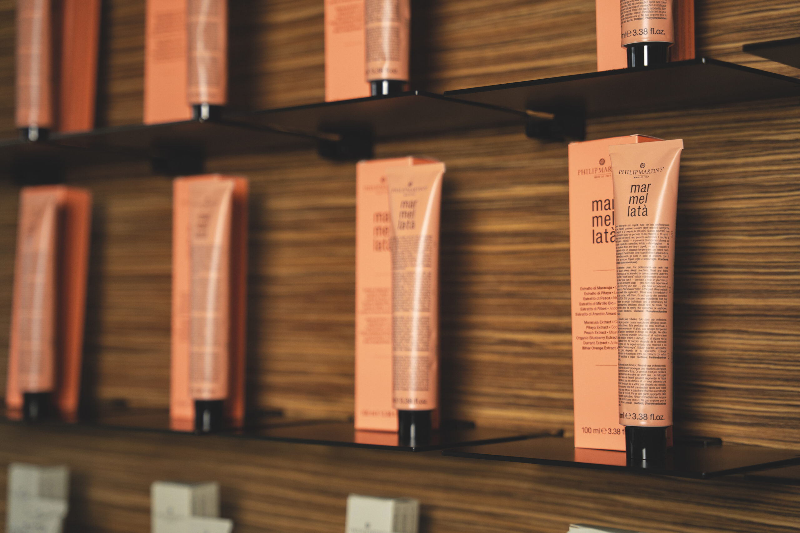 Row of pink cosmetic tubes on wooden display shelves in a store setting.