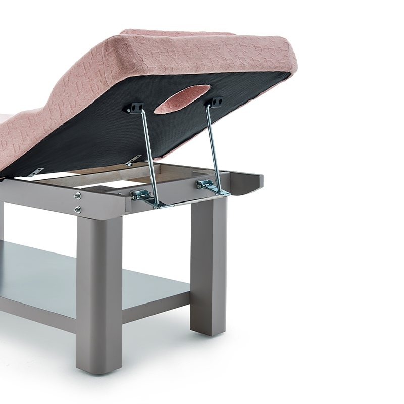 1png โ Rapple Massage table with pink quilted upholstery and an elevated back section, showing metal support arms and a lower shelf.