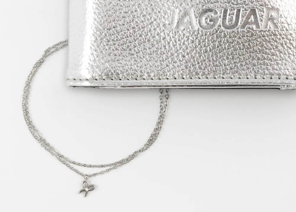 Close-up of a silver textured clutch with a thin silver chain and a small butterfly charm hanging from it