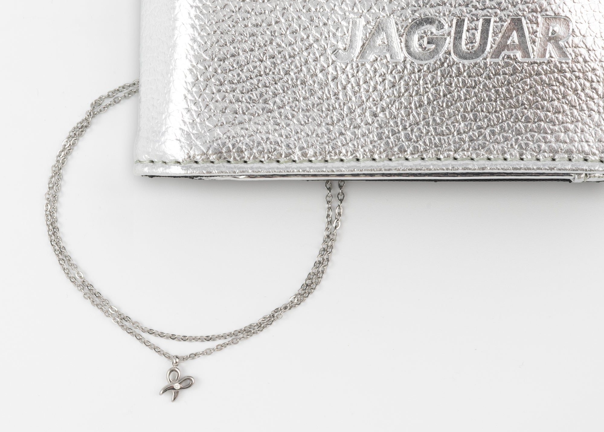 Euphorie-Kette-Detail โ Rapple Close-up of a silver textured clutch with a thin silver chain and a small butterfly charm hanging from it